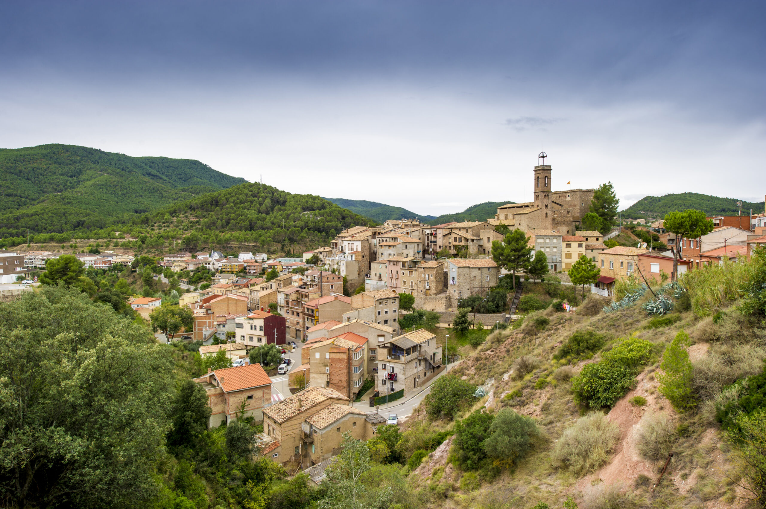 Súria Vista panoràmica del nucli antic de Súria, amb un conjunt de cases de pedra i el campanar de l'església del Roser.